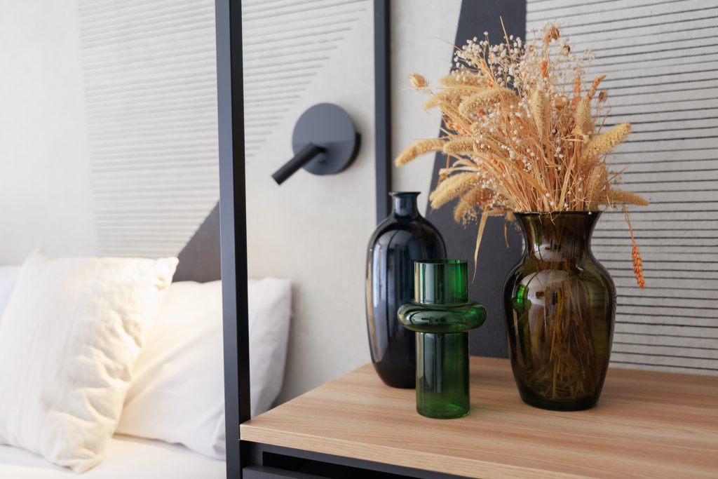 Wood-tone bedside shelf with decorative vases in a Gavà apartment.