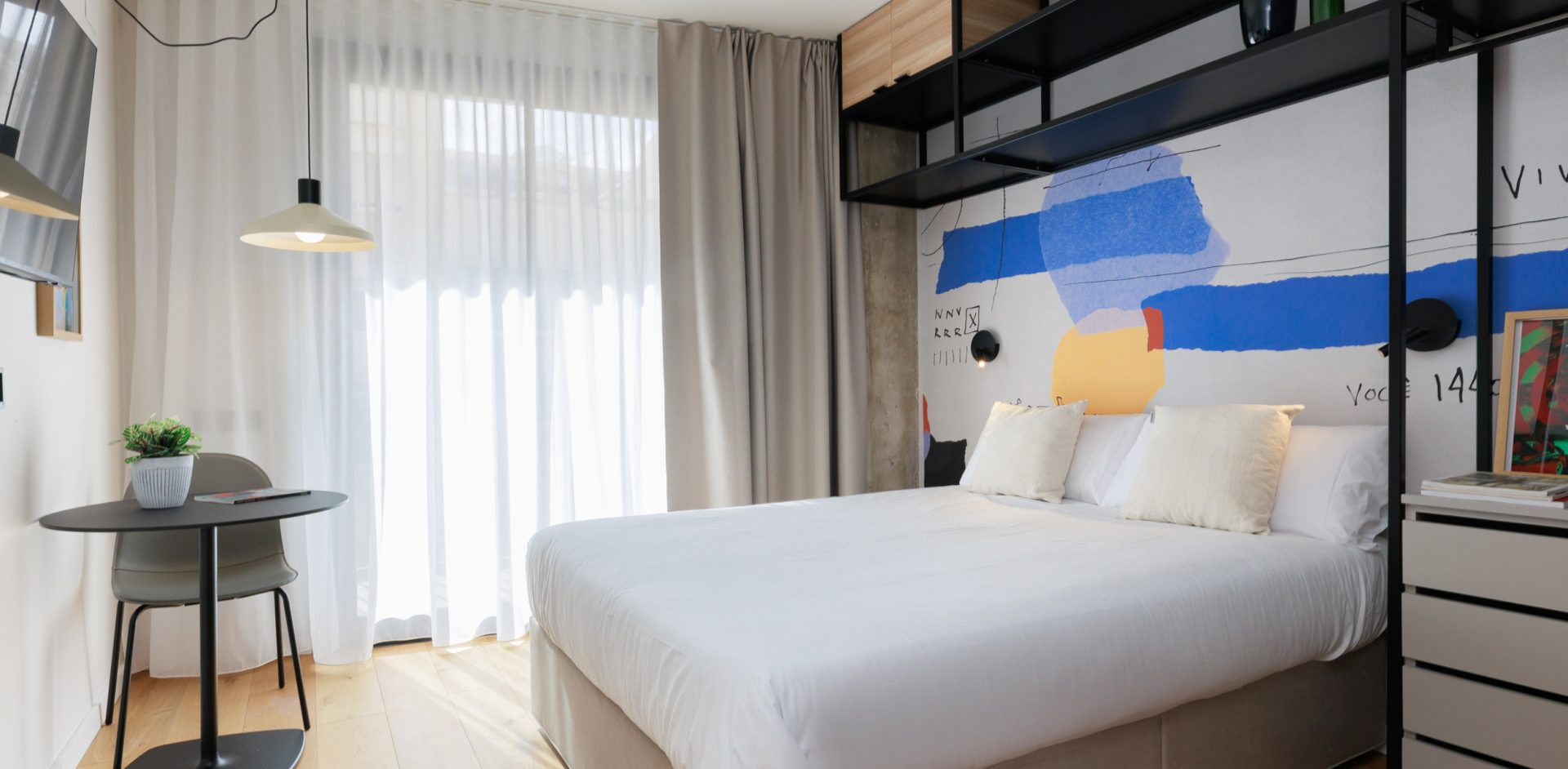 Gavà studio with abstract wall art, a double bed and a dining table by the window.