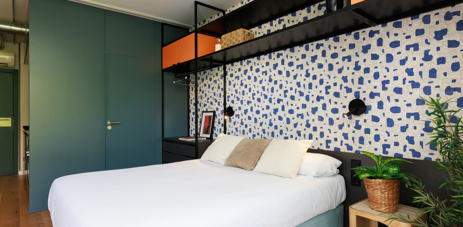 Gavà bedroom with green cabinetry, open shelving and a blue patterned wall.